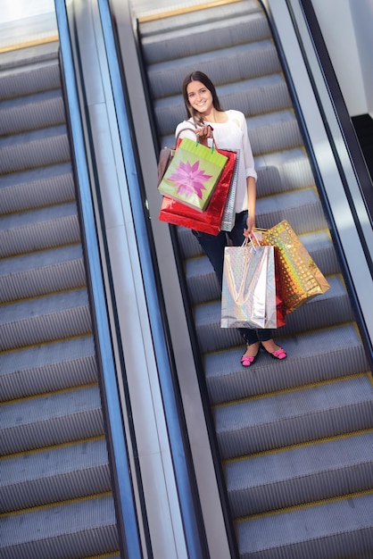 Felice giovane donna su scalatori in un centro commerciale con borse regalo di moda colorate