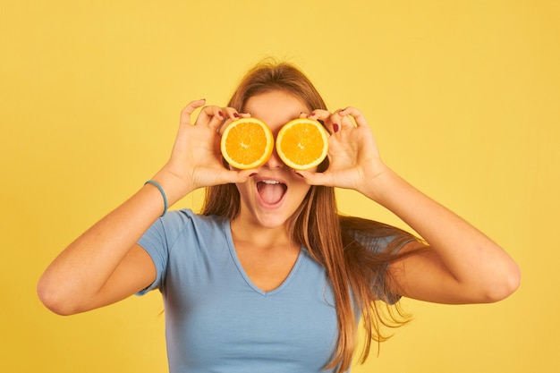 Felice giovane donna utilizzando arance come bicchieri su un giallo