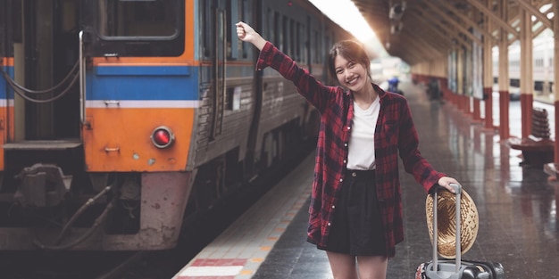 Felice giovane donna viaggiatore che cerca un amico che pianifica un viaggio alla stazione ferroviaria Concetto di stile di vita estivo e di viaggio
