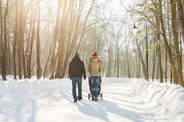 Felice giovane famiglia che cammina nel parco in inverno. I genitori portano il bambino in un passeggino attraverso la neve.