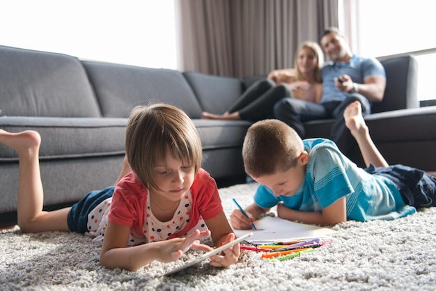 Felice giovane famiglia che gioca insieme a casa sul pavimento utilizzando un tablet e un set da disegno per bambini