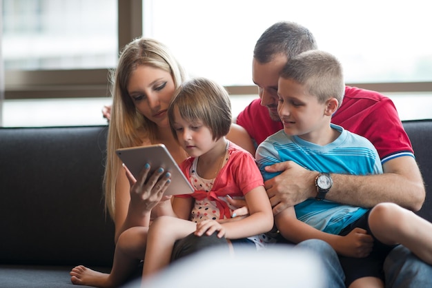 Felice giovane famiglia che gioca insieme al tablet a casa seduto sul divano