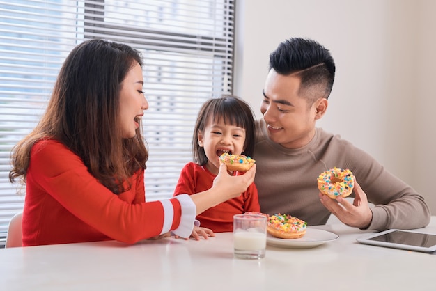 Felice giovane famiglia con bambini che si godono la colazione in una sala da pranzo bianca e soleggiata con una grande finestra con vista sul giardino