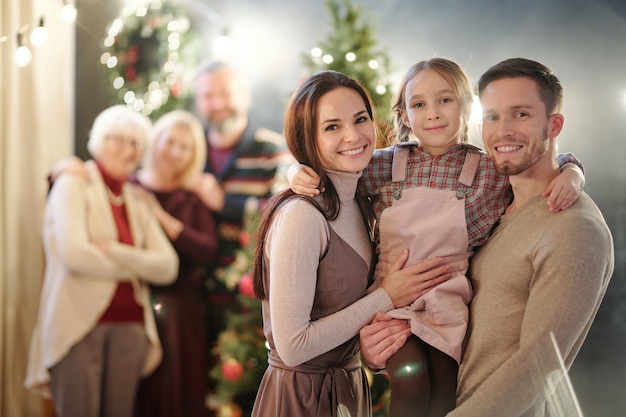 Felice giovane famiglia di tre persone in piedi con adulti maturi da albero di Natale