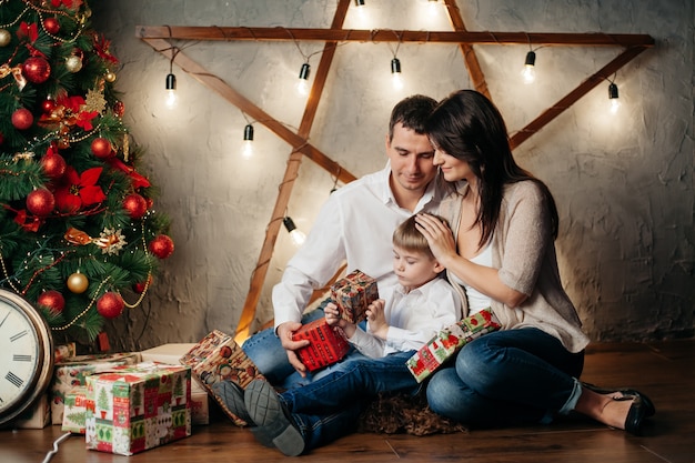 Felice giovane famiglia in decorazioni natalizie, mamma, papà e ragazzino vicino all'albero di Natale con regali vicino