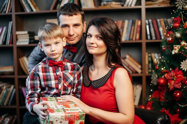Felice giovane famiglia in decorazioni natalizie, mamma, papà e ragazzino vicino all'albero di Natale con regali vicino