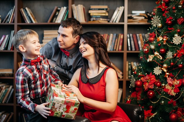 Felice giovane famiglia in decorazioni natalizie, mamma, papà e ragazzino vicino all'albero di Natale con regali vicino