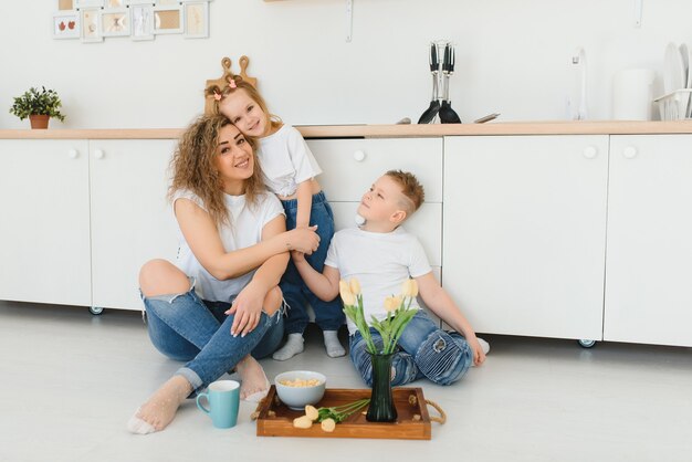 Felice giovane famiglia, mamma con bambini piccoli si siede sul pavimento in cucina