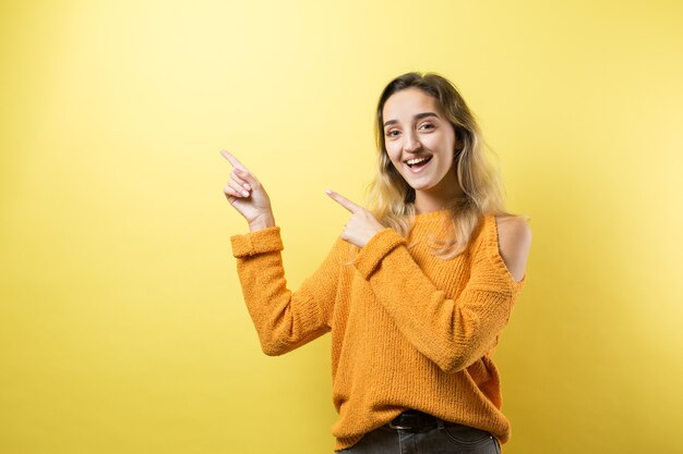 Felice giovane femmina caucasica in un maglione giallo che punta le dita lontano.