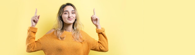 Felice giovane femmina caucasica in un maglione giallo che punta le dita lontano.