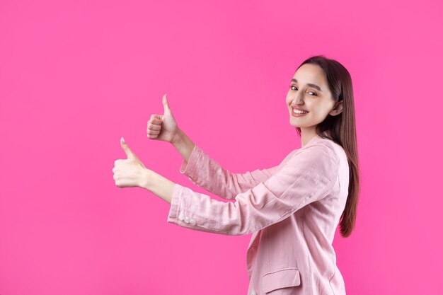 Felice giovane femmina caucasica in una giacca rosa che fa il segno del pollice in su e sorride Buon lavoro e rispetto