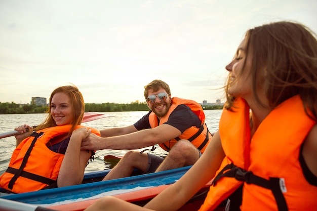 Felice giovane gruppo caucasico di amici in kayak sul fiume con il tramonto sullo sfondo. Divertirsi in attività per il tempo libero. Felice modello maschile e femminile che ride sul kayak. Sport, concetto di relazioni.