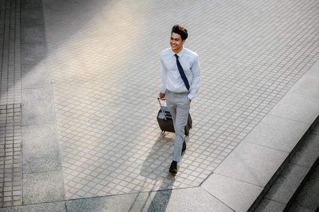 Felice giovane imprenditore a piedi con la valigia in città. Uomo moderno in viaggio d'affari. Veduta dall'alto.