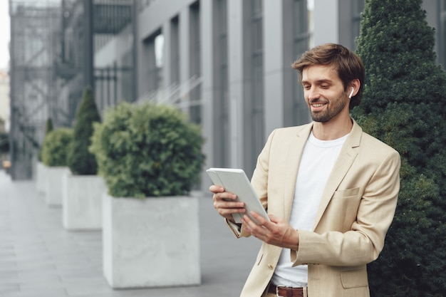 Felice giovane imprenditore vestito in abito alla moda avente conversazione di lavoro tramite videochiamata su tavoletta digitale