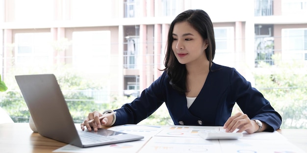 Felice giovane imprenditrice asiatica seduta sul suo posto di lavoro in ufficio Giovane donna che lavora al computer portatile in ufficio