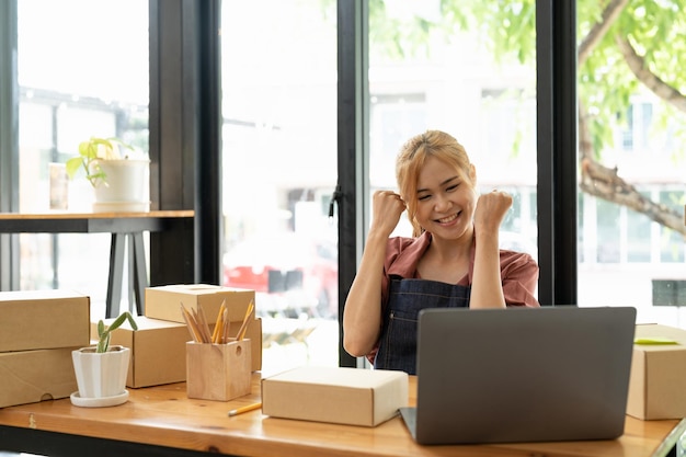 Felice giovane imprenditrice asiatica Sorriso per il successo delle vendite dopo aver controllato l'ordine dal negozio di shopping online in uno smartphone a casa dell'ufficio Concetto di attività commerciale online ed eCommerce