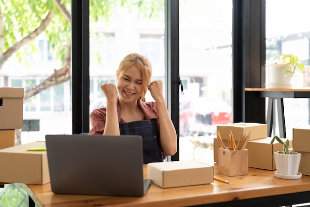 Felice giovane imprenditrice asiatica Sorriso per il successo delle vendite dopo aver controllato l'ordine dal negozio di shopping online in uno smartphone a casa dell'ufficio Concetto di attività commerciale online ed eCommerce