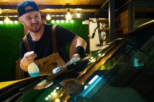 Felice giovane lavoratore del servizio di manutenzione che pulisce il parabrezza dell'auto