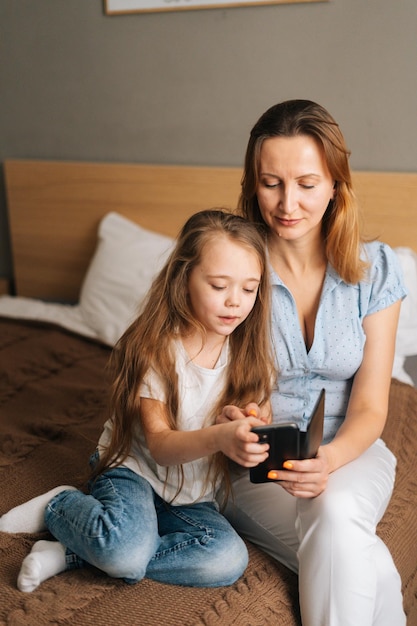 Felice giovane madre che abbraccia la figlia in età prescolare insieme navigando e navigando in Internet sul telefono cellulare in chat durante la videochiamata