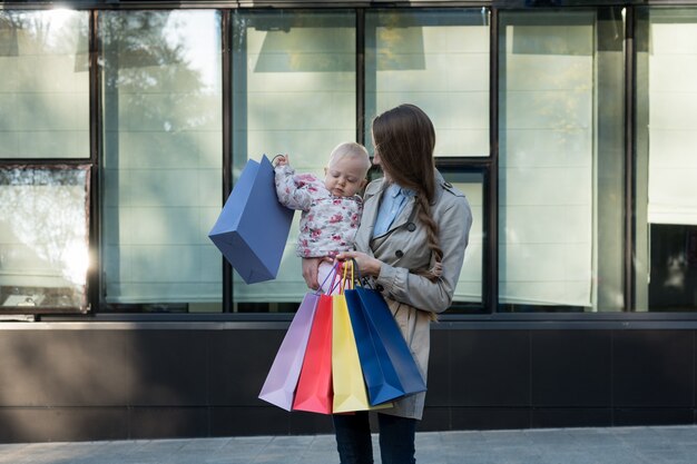 Felice giovane madre con figlia piccola sulle braccia e borse della spesa in mano. Giornata di shopping. Centro commerciale