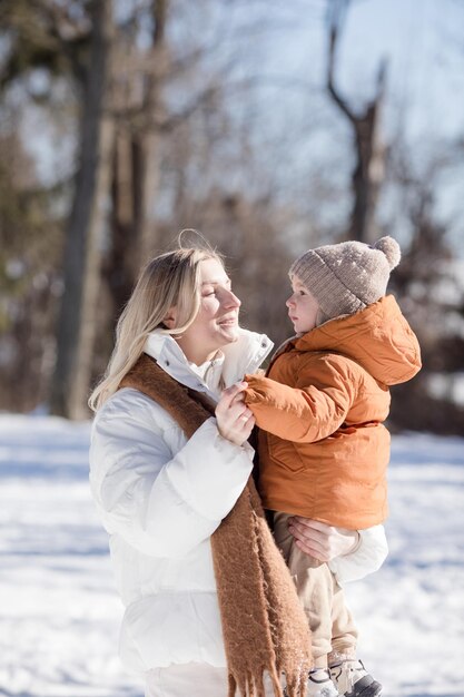 Felice giovane madre con figlio a passeggiare nel parco invernale Ritratto di famiglia felice all'aperto Figlio che getta neve in madre