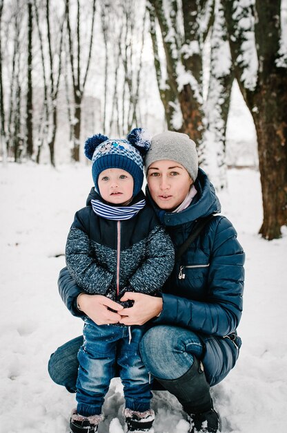 Felice giovane madre con figlio a piedi nel parco invernale. Avvicinamento. Ritratto famiglia felice all'aperto.