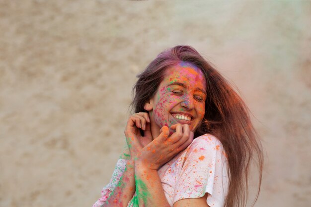 Felice giovane modella con il vento tra i capelli che celebra il festival dei colori di Holi nel deserto. Spazio per il testo