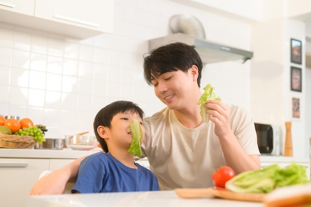 Felice giovane padre e figlio asiatici che mangiano cibo sano in cucina a casa