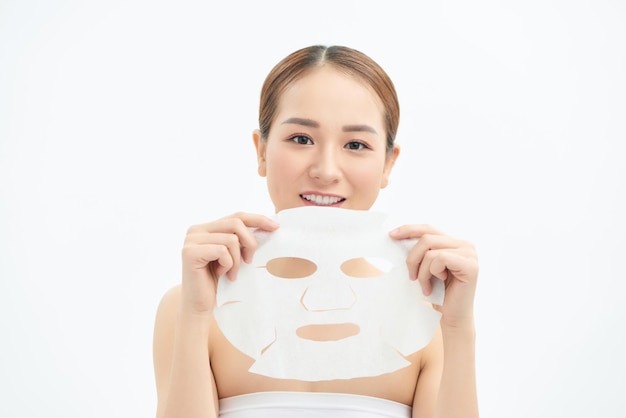 Felice giovane ragazza asiatica con maschera facciale isolata su sfondo bianco