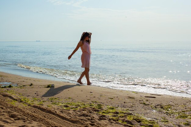 Felice giovane ragazza in un vestito rosa e occhiali scuri andando sulle onde del mare a mezzogiorno Rilassante vacanza indimenticabile in mare in estate Godersi l'estate Giocare in acqua