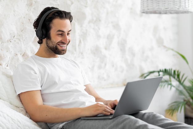 Felice giovane seduto sul letto utilizzando il computer