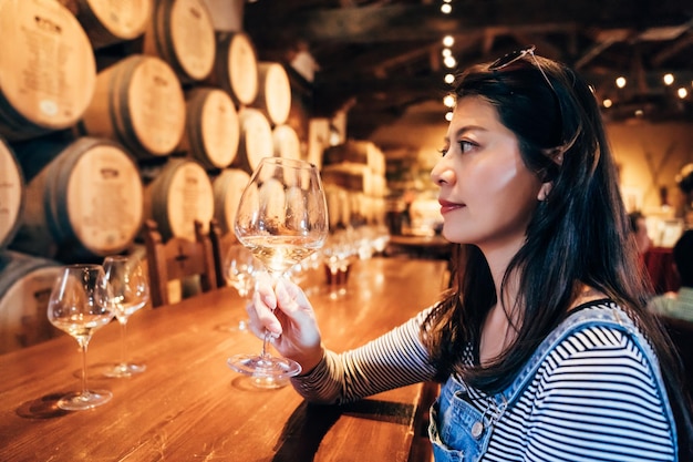 Felice giovane signora asiatica degustazione di vino seduto nel ristorante nella valle di napa da solo. elegante steward professionista del vino che lavora facendo il suo lavoro nel bar al coperto. locale cantina interrata