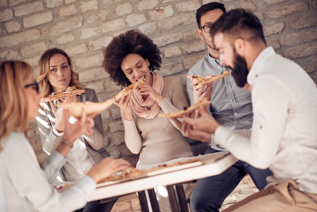 Felice giovane squadra di affari che mangia pizza in ufficio