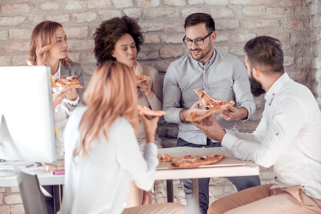 Felice giovane squadra di affari che mangia pizza in ufficio