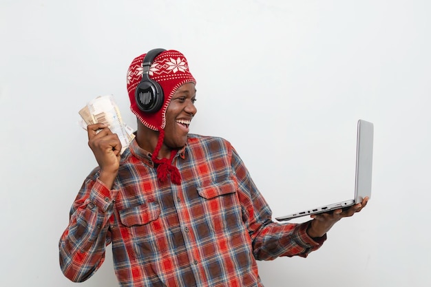 Felice giovane studente africano nero eccitato che tiene contanti mentre sorride guardando il portatile a portata di mano