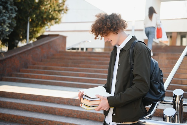 Felice giovane studente ragazzo in una giornata di sole che legge un libro e studia ed è molto sorridente