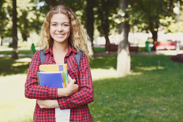 Felice giovane studentessa in piedi nel parco con lo zaino dietro le spalle. Tecnologia, comunicazione, istruzione e concetto di lavoro a distanza, spazio di copia