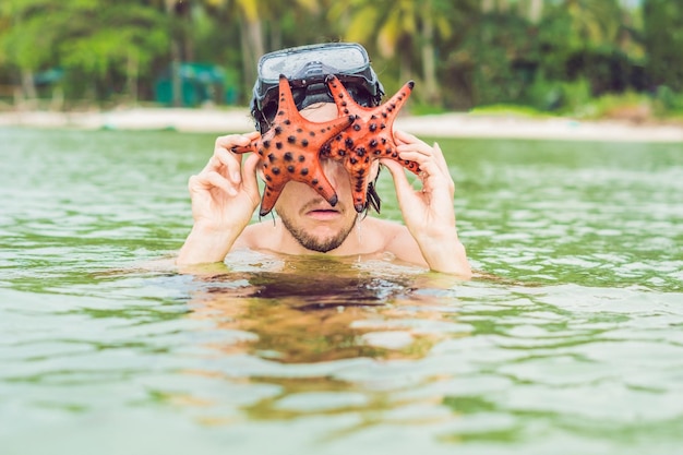 Felice giovane subacqueo che tiene la stella di mare, sorridente, guardando la telecamera