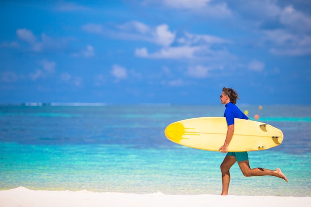 Felice giovane surf uomo che corre in spiaggia con una tavola da surf