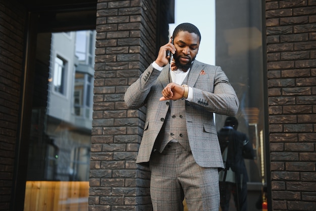 Felice giovane uomo africano in abbigliamento formale, parlando al telefono cellulare e sorridente, mentre in piedi all'aperto