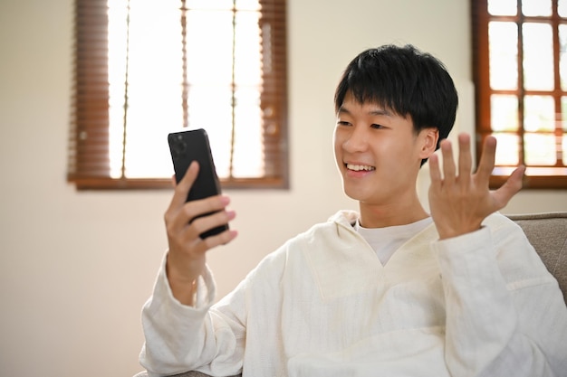 Felice giovane uomo asiatico che legge blog online o guarda clip divertenti usando il suo telefono
