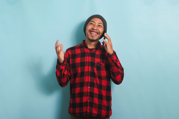 Felice giovane uomo asiatico sta ridendo sentendo barzellette divertenti sulla sua telefonata isolata su sfondo blu