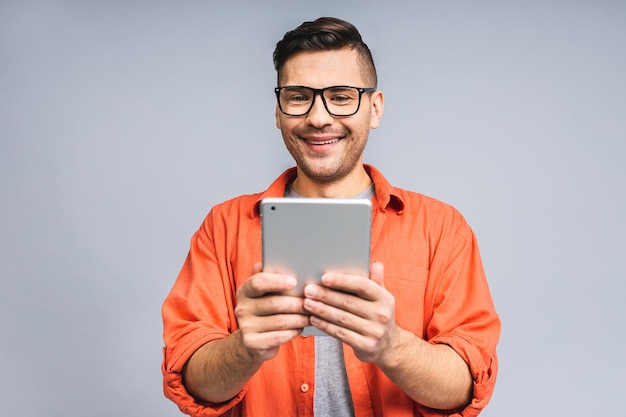 Felice giovane uomo barbuto in piedi casual e utilizzando tablet isolato su sfondo bianco grigio