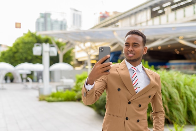 Felice giovane uomo d'affari africano bello prendendo selfie in città