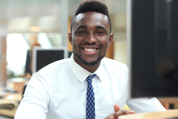 Felice giovane uomo d'affari afroamericano che guarda l'obbiettivo sul posto di lavoro in ufficio.