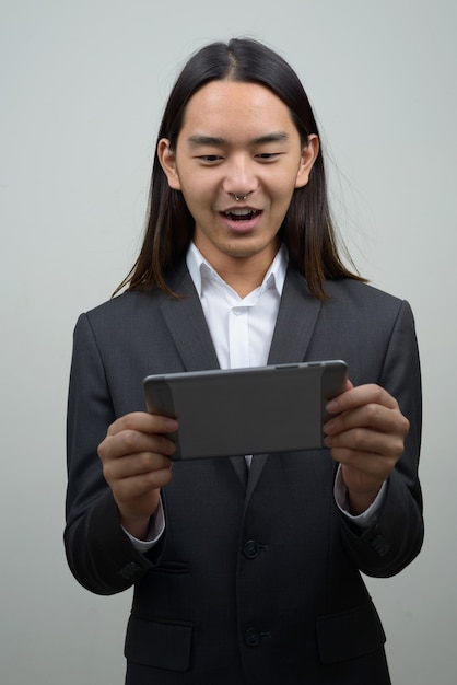 Felice giovane uomo d'affari asiatico con i capelli lunghi che sembra sorpreso durante l'utilizzo di tavoletta digitale
