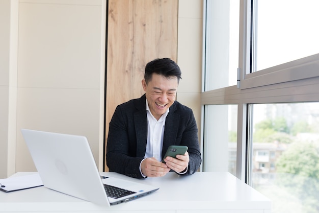 felice giovane uomo d'affari asiatico in ufficio guardando il cellulare