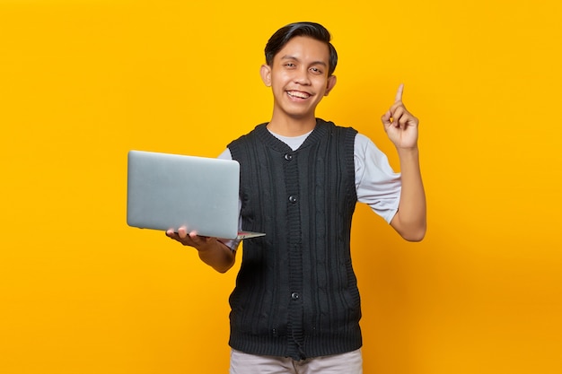 Felice giovane uomo d'affari bello che ha un'idea creativa mentre tiene in mano un computer portatile su sfondo giallo