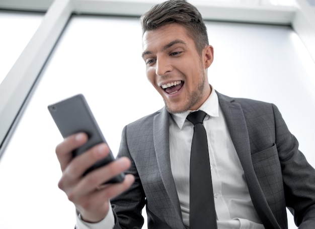 Felice giovane uomo d'affari che legge un messaggio di testo sul telefono cellulare