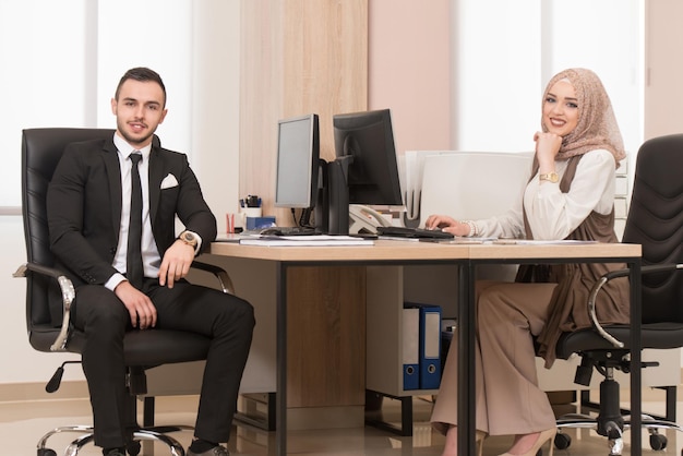 Felice giovane uomo d'affari e donna musulmana lavorano in un ufficio moderno sul computer